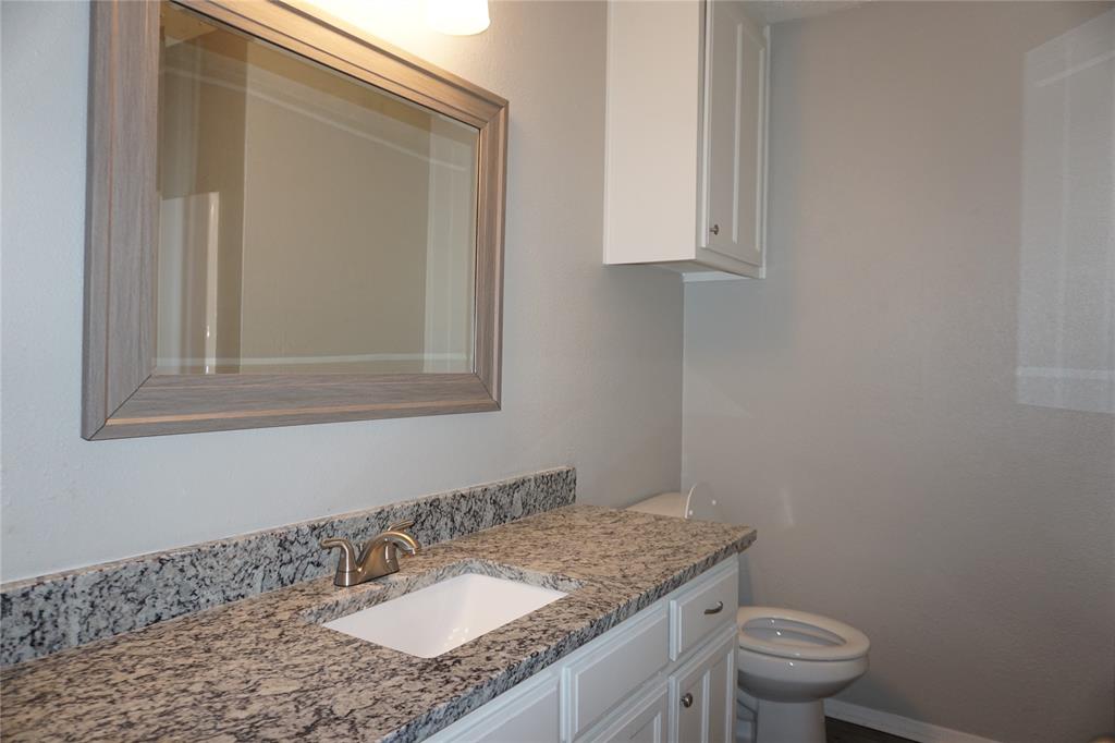 6412 Fairview Drive Watauga, TX 76148 - Photo 11 of 14 a bathroom with a granite countertop sink a toilet and a mirror