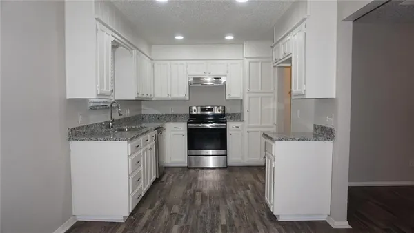 a kitchen with granite countertop a refrigerator and white cabinets