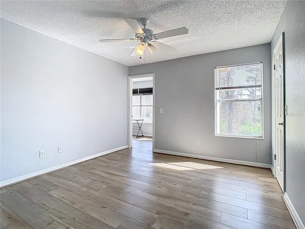 an empty room with wooden floor chandelier fan and windows