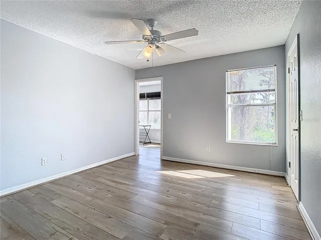 an empty room with wooden floor chandelier fan and windows