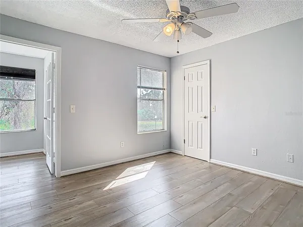 an empty room with wooden floor chandelier fan and windows