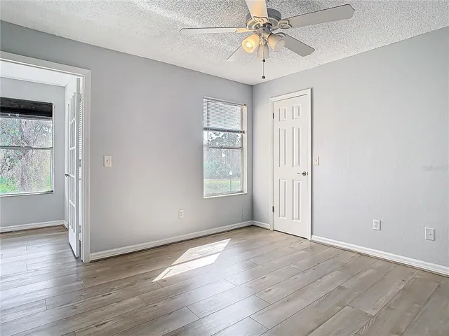 an empty room with wooden floor chandelier fan and windows
