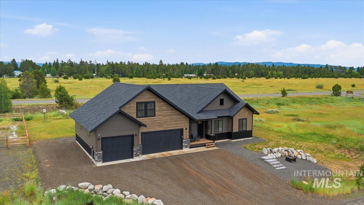 13152 Hawks Bay Road Donnelly, ID 83615 - Photo 26 of 29 Modern ranch-style home featuring a dark shingle roof, mixed-material siding, an attached three-car garage, gravel driveway, and an outdoor fire pit area
