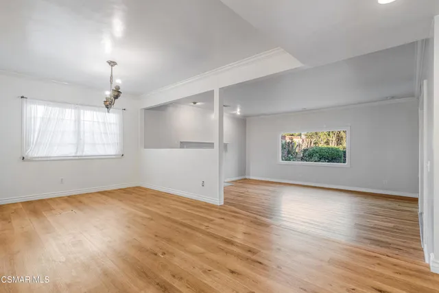 an empty room with wooden floor chandelier and windows