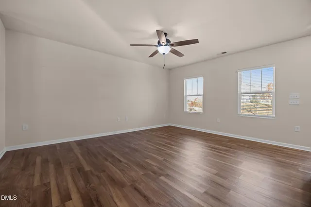 an empty room with wooden floor window and ceiling fan