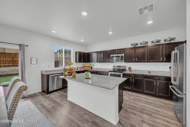 a kitchen with stainless steel appliances kitchen island granite countertop a stove top oven a sink dishwasher a refrigerator and white cabinets with wooden floor
