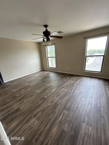 an empty room with wooden floor chandelier fan and windows