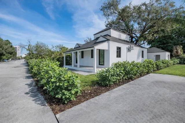 a white house with a small yard plants and large tree