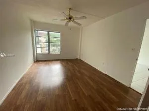 an empty room with wooden floor fan and windows