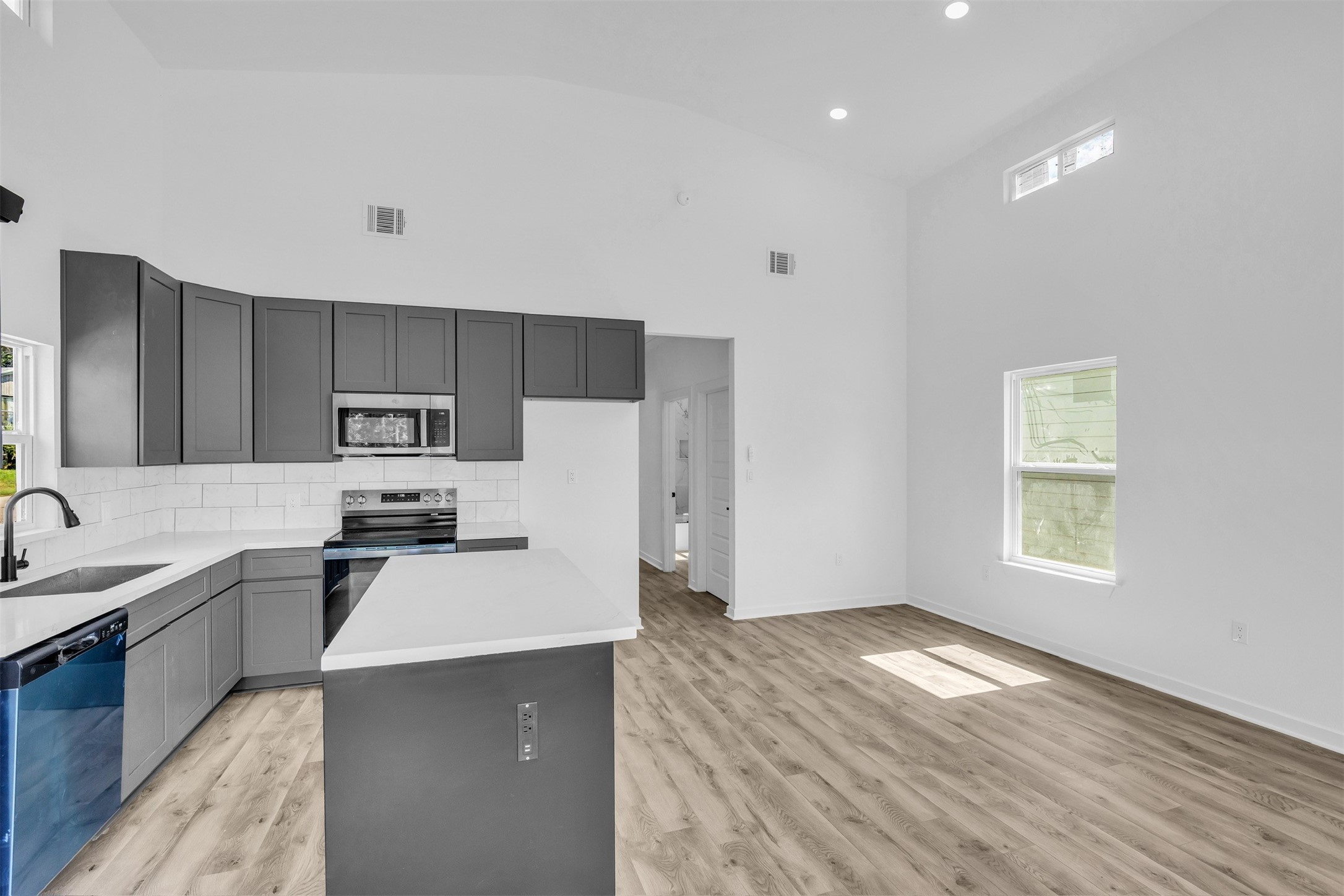 117 Rain Forest Road Onalaska, TX 77360 - Photo 12 of 30 Experience modern living in this bright, open-concept kitchen featuring sleek gray cabinetry, stainless steel appliances, and elegant wood flooring.