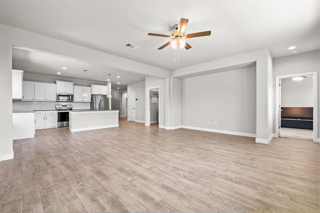1840 Ruffian Road Granbury, TX 76049 - Photo 7 of 33 Open-concept living space featuring wood-finish flooring, a kitchen with white cabinetry, stainless steel appliances, and a breakfast bar
