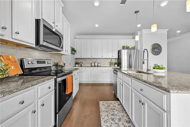a white kitchen with stainless steel appliances granite countertop a stove a sink and a microwave