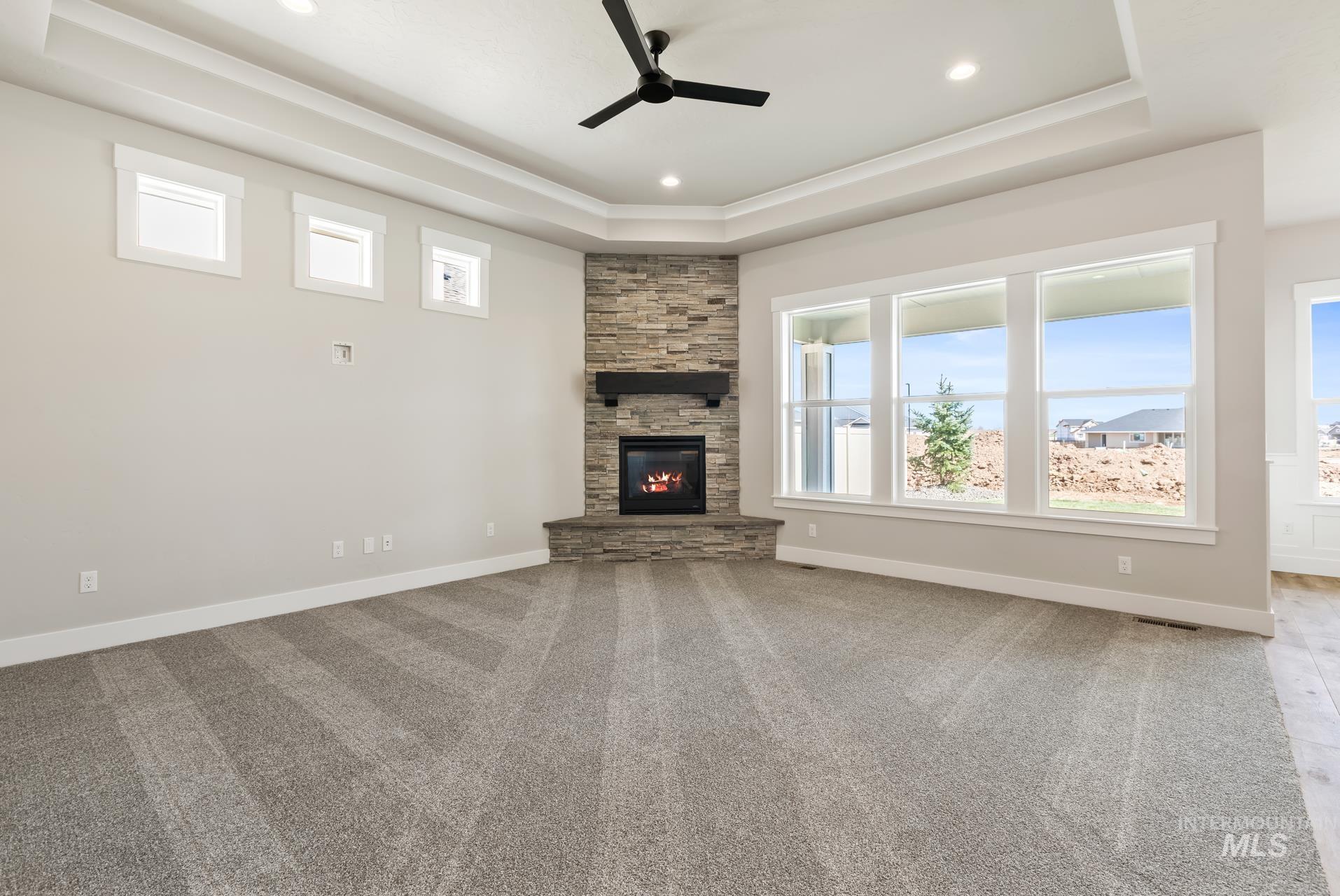 385 South Strut Way Boise, ID 83716 - Photo 12 of 30 Unfurnished living room featuring a tray ceiling, light colored carpet, ceiling fan, a fireplace, and recessed lighting
