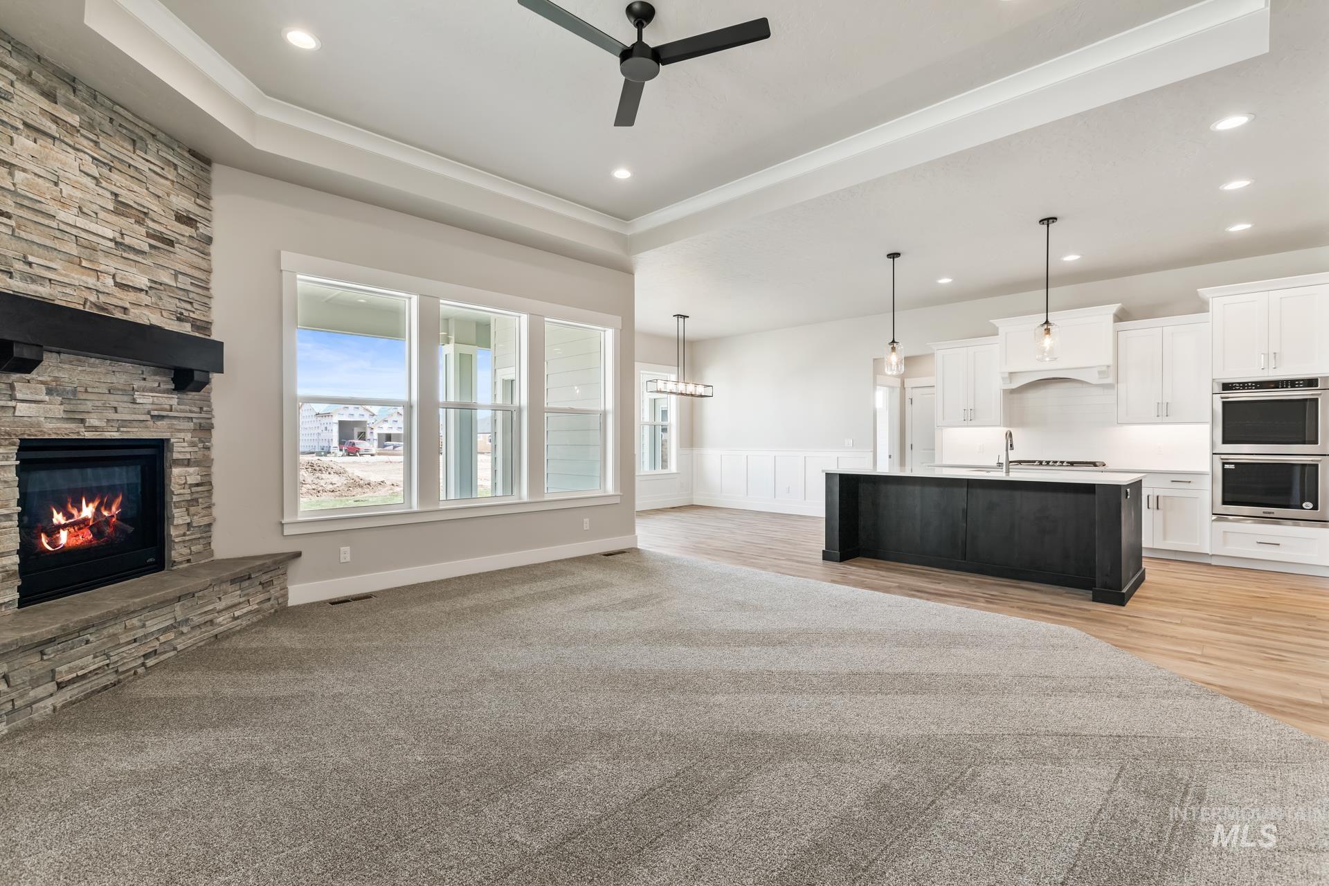 385 South Strut Way Boise, ID 83716 - Photo 13 of 30 Unfurnished living room with a raised ceiling, a ceiling fan, a stone fireplace, light carpet, and a wainscoted wall
