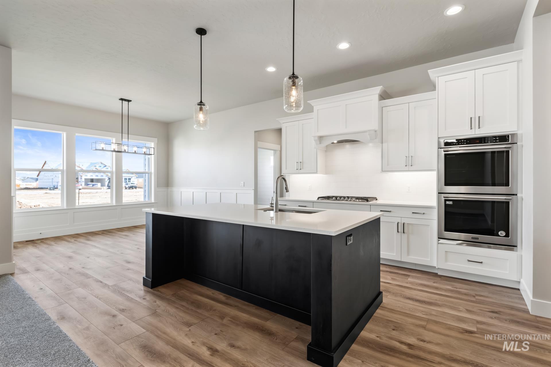 385 South Strut Way Boise, ID 83716 - Photo 16 of 30 Kitchen with white cabinets, decorative light fixtures, stainless steel appliances, light wood-style flooring, and an island with sink