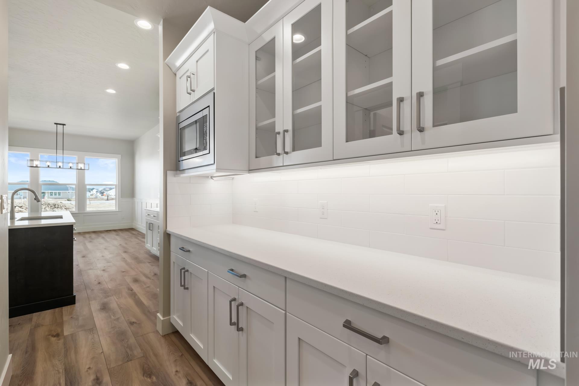 385 South Strut Way Boise, ID 83716 - Photo 17 of 30 Bar area featuring light wood-style floors, white cabinetry, light stone counters, glass insert cabinets, and recessed lighting