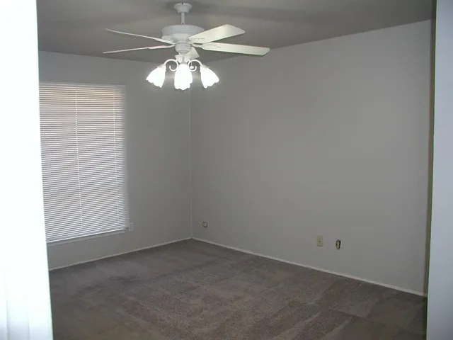 an empty room with a chandelier fan and windows