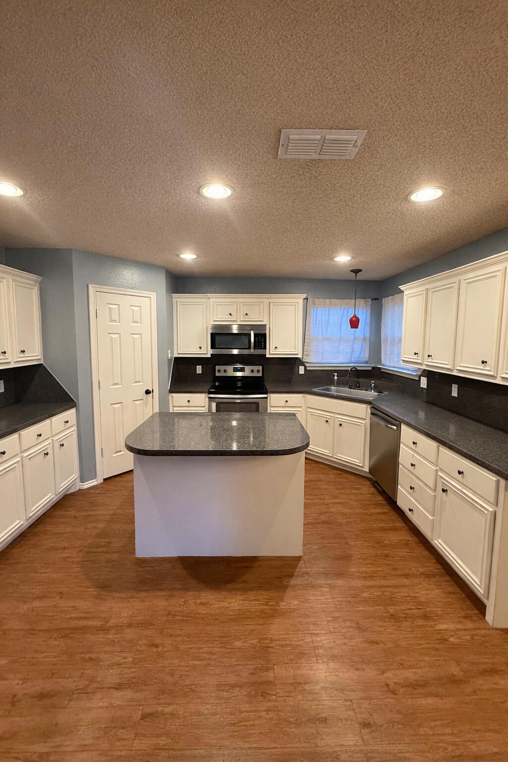 6115 100th Street Lubbock, TX 79424 - Photo 11 of 27 a large kitchen with stainless steel appliances granite countertop a stove a sink dishwasher and a microwave oven with white cabinets