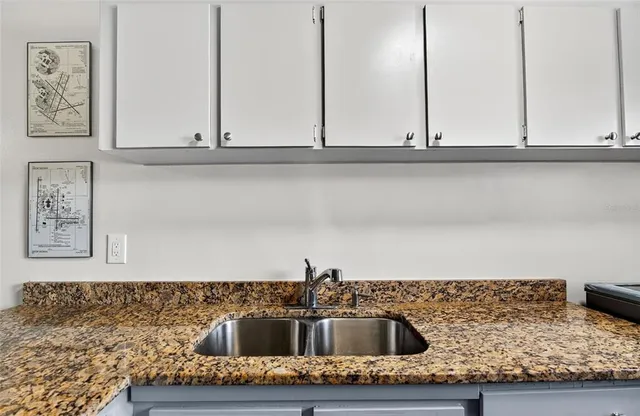 a kitchen sink with granite countertop white cabinets and a sink