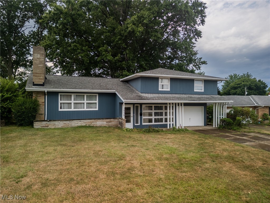View of front of property featuring a garage, concrete driveway, a front lawn, and a chimney