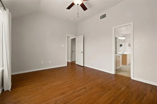 an empty room with wooden floor ceiling fan and windows