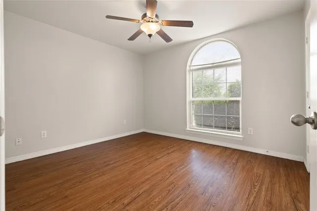 an empty room with wooden floor chandelier fan and windows