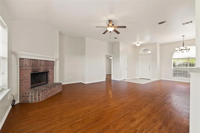 a view of an empty room with wooden floor fireplace and a window
