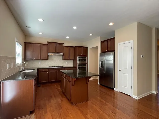 a kitchen with stainless steel appliances granite countertop a refrigerator a sink dishwasher a stove and a refrigerator with wooden floor