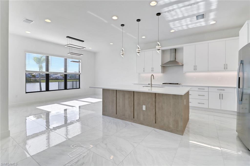 20458 Fair Oak Lane Estero, FL 33928 - Photo 7 of 40 Kitchen featuring white cabinetry, a center island with sink, and wall chimney range hood