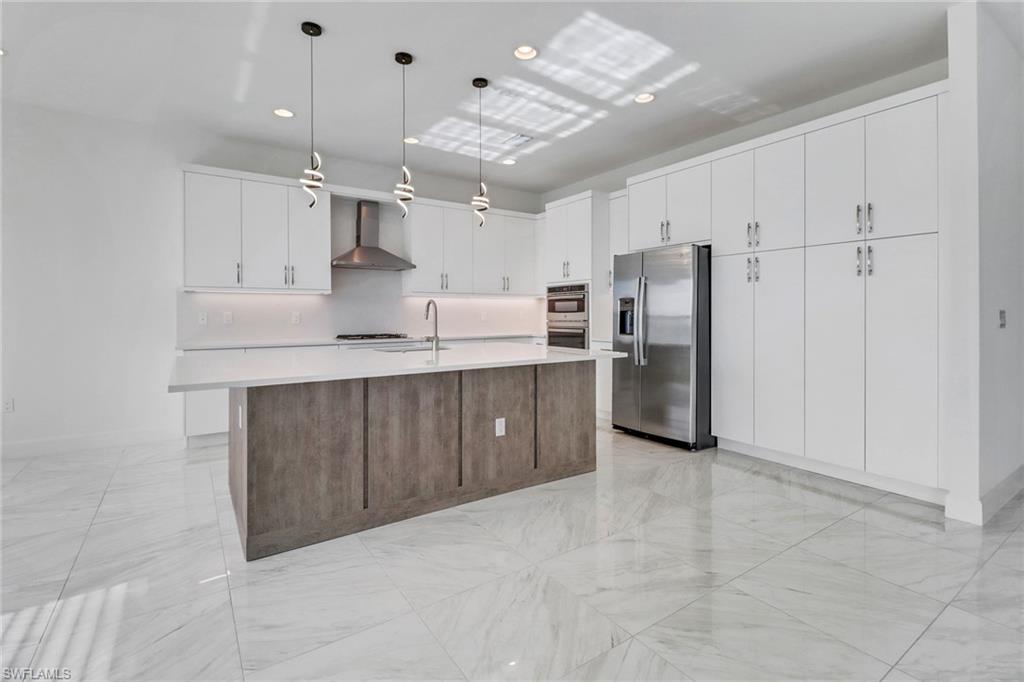 20458 Fair Oak Lane Estero, FL 33928 - Photo 8 of 40 Kitchen with appliances with stainless steel finishes, white cabinetry, hanging light fixtures, and wall chimney exhaust hood