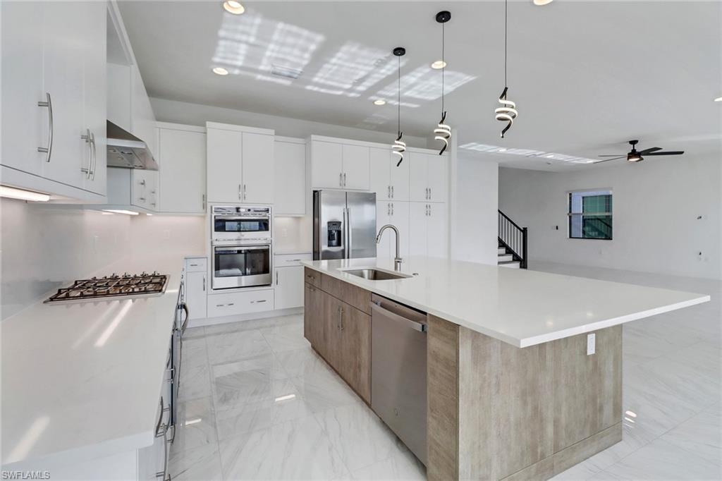 20458 Fair Oak Lane Estero, FL 33928 - Photo 9 of 40 Kitchen featuring appliances with stainless steel finishes, a spacious island, wall chimney range hood, white cabinets, and hanging light fixtures