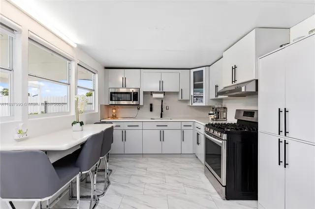 a kitchen with stainless steel appliances granite countertop a sink a stove a refrigerator cabinets and a dining table with wooden floor