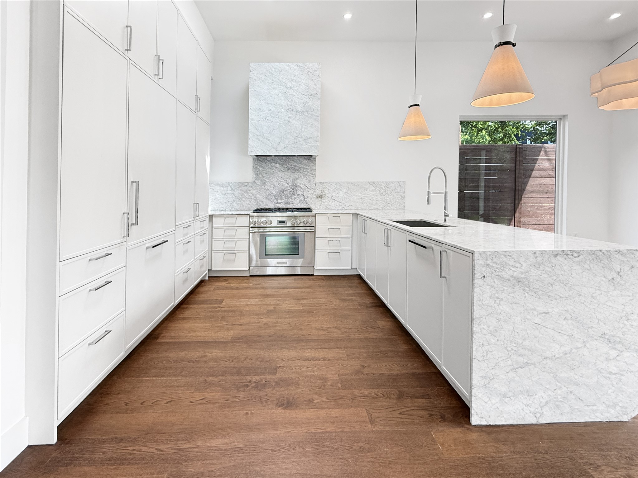 127 Frederick Street Austin, TX 78704 - Photo 7 of 34 Sleek kitchen featuring an oversized island with waterfall edge, white cabinetry, integrated stainless steel appliances, marble countertops, and rich wood-finish flooring