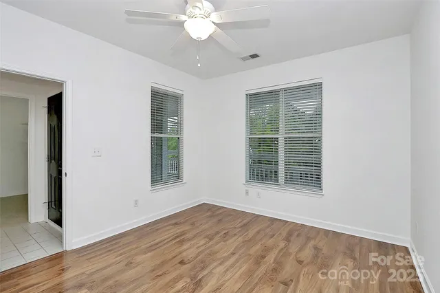 an empty room with wooden floor fan and windows