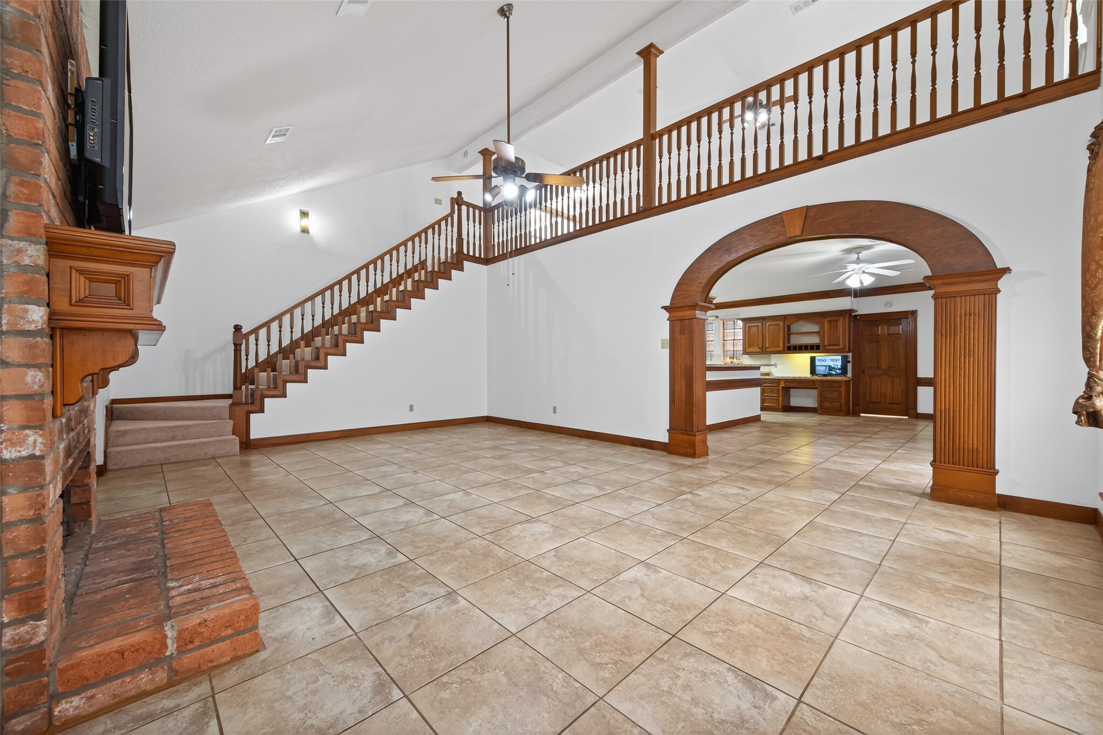 17315 Rothko Lane Spring, TX 77379 - Photo 17 of 50 Expansive family room showcasing soaring ceilings, a striking staircase with wood railing, and a cozy brick fireplace. This spacious open concept space features durable tile flooring, elegant architectural archways, and seamless flow into adjacent areas.
