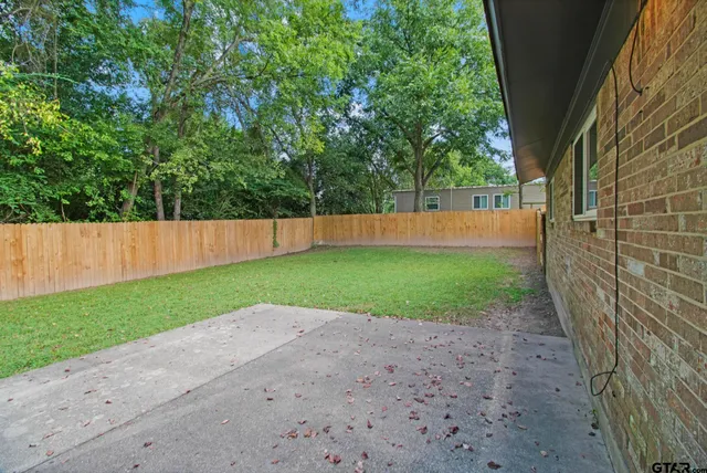 a view of a backyard with large trees and wooden fence