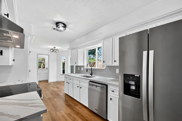 a large kitchen with a refrigerator a sink dishwasher and white cabinets with wooden floor