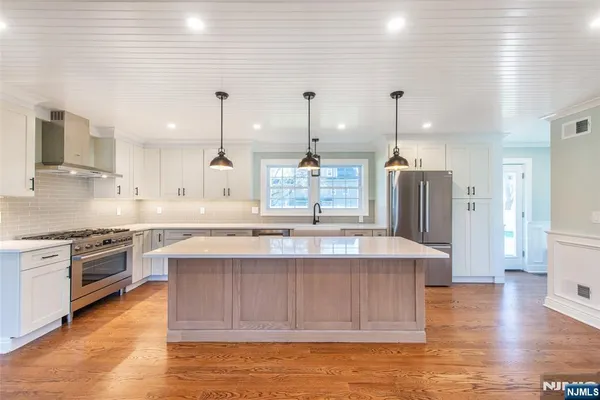 a kitchen with stainless steel appliances granite countertop a sink a stove a refrigerator and island with wooden floor