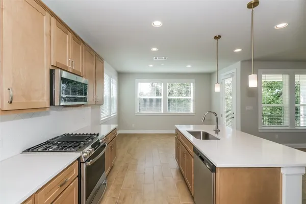 a view of a kitchen with kitchen island a large counter top space a sink stainless steel appliances and cabinets