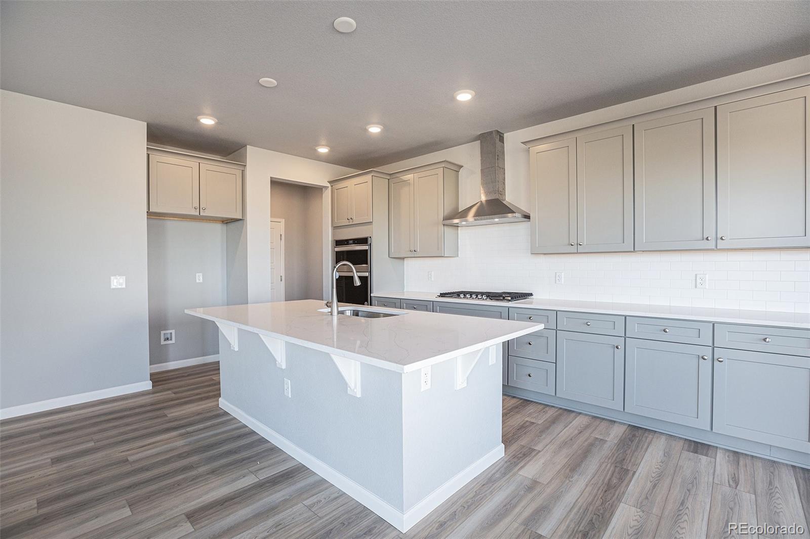 15965 Stringhalt Way Parker, CO 80134 - Photo 9 of 33 a large white kitchen with wooden floors and white cabinets