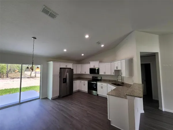 a open kitchen with stainless steel appliances granite countertop a refrigerator a sink dishwasher a stove and a large countertops with wooden floor