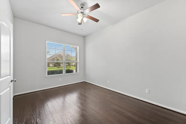 an empty room with wooden floor chandelier fan and windows