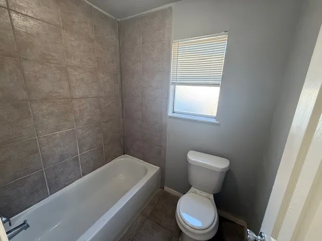 a white toilet sitting next to a bath tub and a window