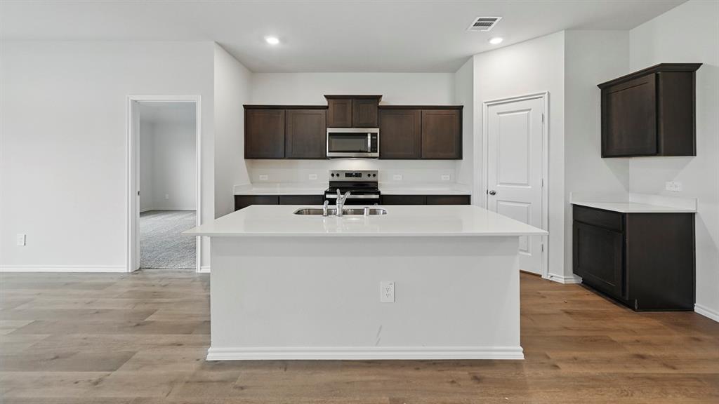 1908 Freeman Street Tyler, TX 75704 - Photo 8 of 30 Kitchen featuring a central island with an undermount sink, dark wood cabinetry, stainless steel appliances, and wood-finish flooring