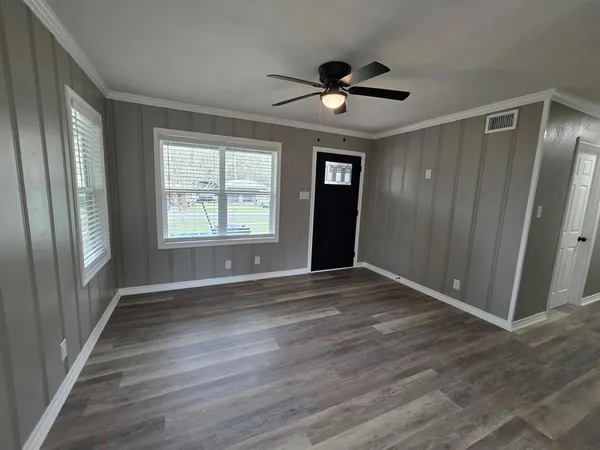 an empty room with wooden floor fan and windows
