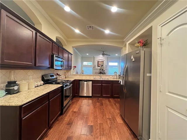 a kitchen with stainless steel appliances granite countertop a refrigerator a sink dishwasher a stove with wooden cabinets and floor