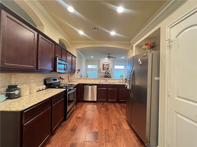 a kitchen with stainless steel appliances granite countertop a refrigerator a sink dishwasher a stove with wooden cabinets and floor