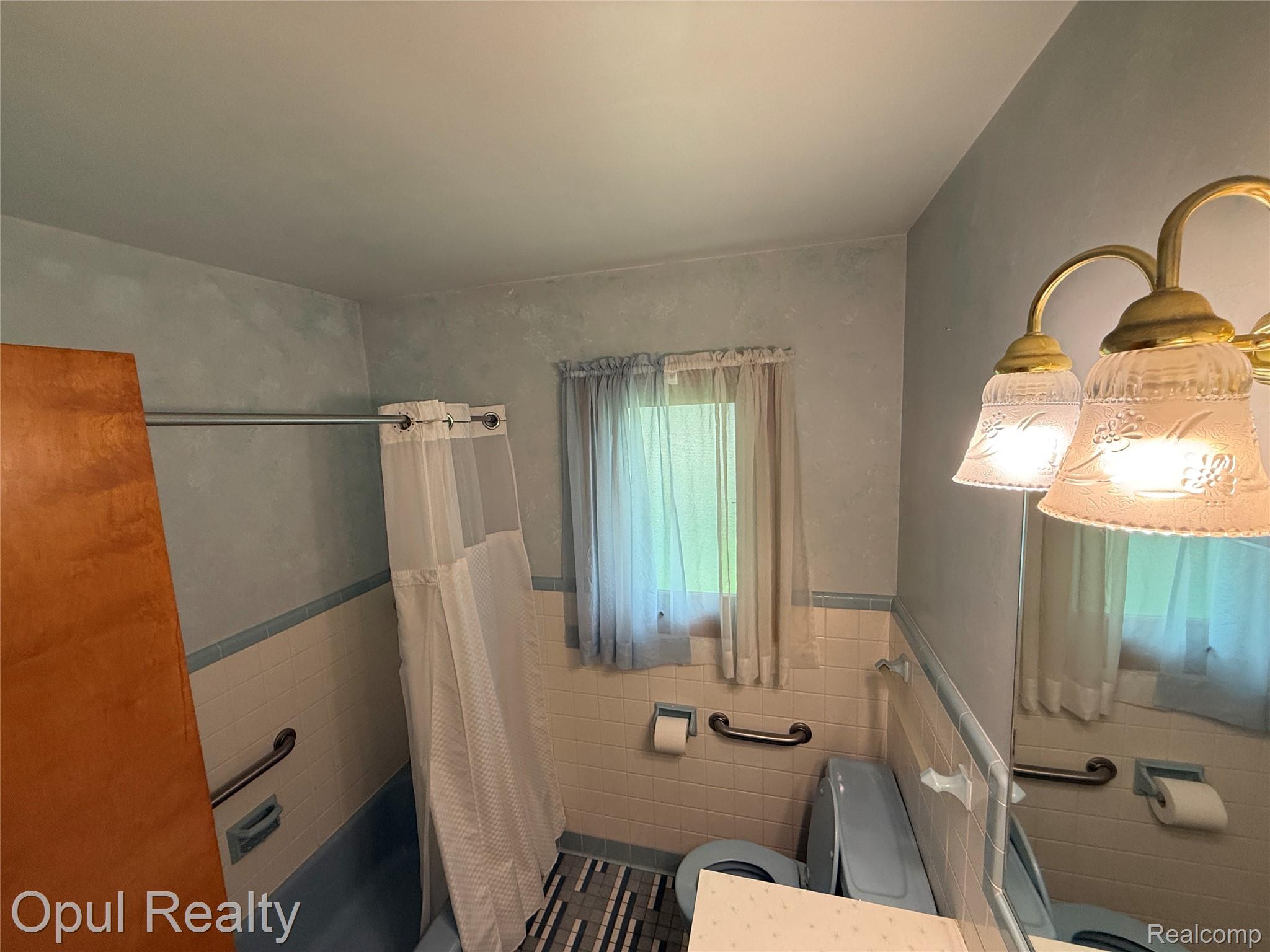 7899 Ida East Road Ida, MI 48140 - Photo 30 of 48 Bathroom featuring blue-tiled walls, a window with sheer curtains, a three-light vanity fixture, and a built-in toilet