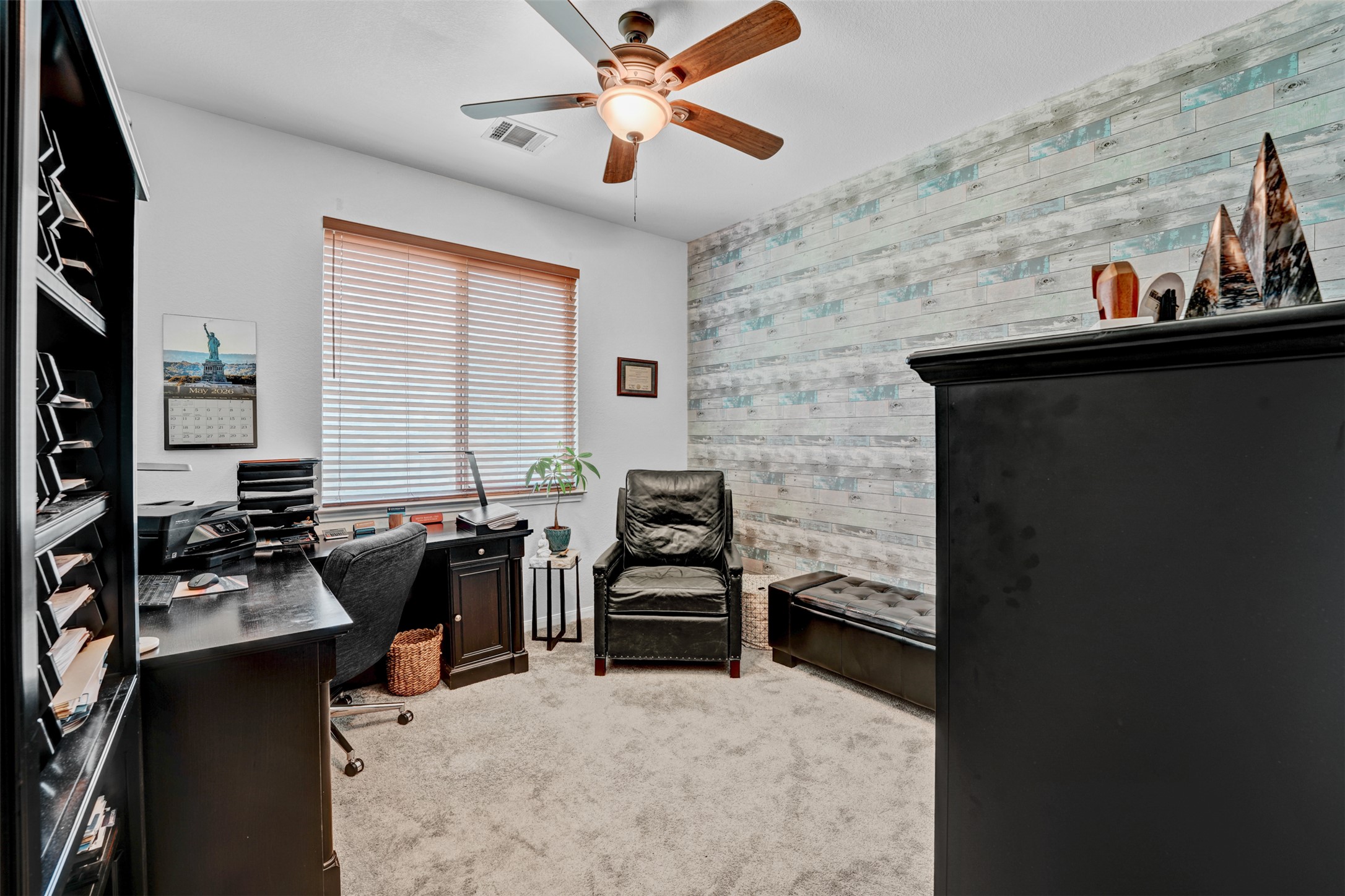 2521 Amen Corner Road Pflugerville, TX 78660 - Photo 27 of 40 Light-filled room featuring a decorative accent wall with a wood-look finish, a ceiling fan with light fixture, and a window with horizontal blinds