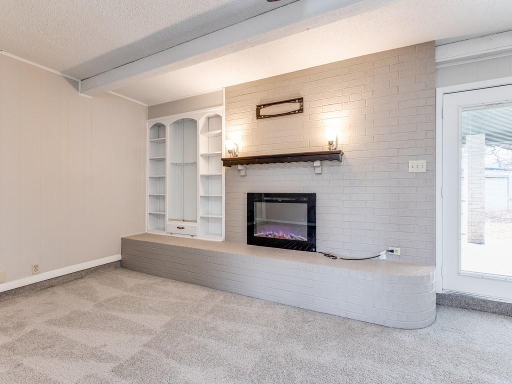 7325 Reed Road Azle, TX 76020 - Photo 16 of 38 Unfurnished living room with carpet flooring, a textured ceiling, a fireplace, built in shelves, and wood walls